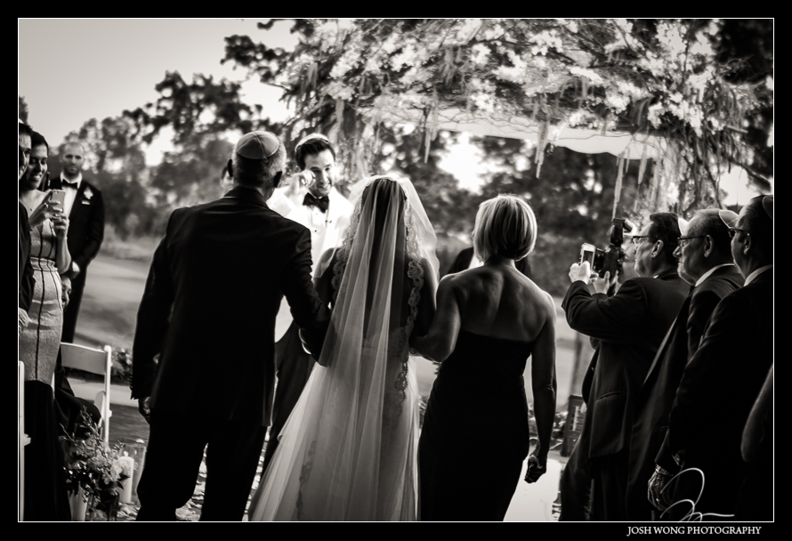 The parents escort their daughter down the aisle in a traditional Jewish wedding.