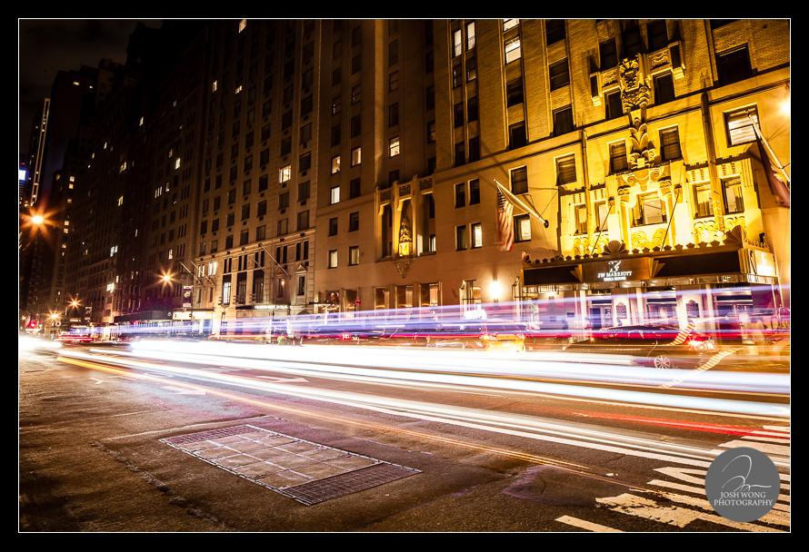 The Essex House at night with the busy streaks of cars flowing by.