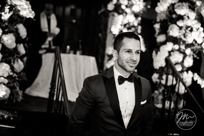 The best wedding candid moments. The groom's excitement builds as he watches his bride emerge escorted by the brides parents. A Jewish wedding at the Temple of Israel in Lawrence, NY by top New York Wedding Photographers Josh Wong Photography