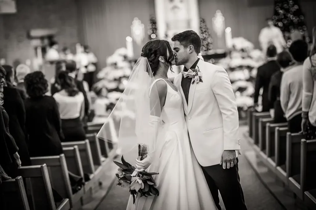 The newlywed couple has a kiss. view from the back pews of St. Joseph Catholic Church in Lincoln Nebraska. photography by Josh Wong